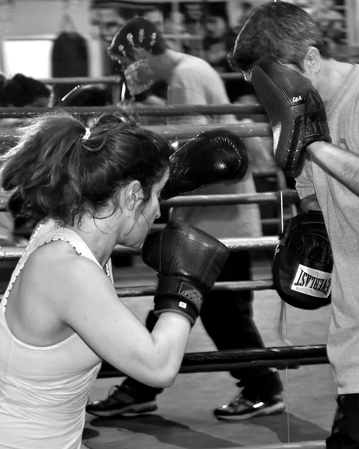 Boxerin in Deckung vor einem Trainer mit Pratzen.
