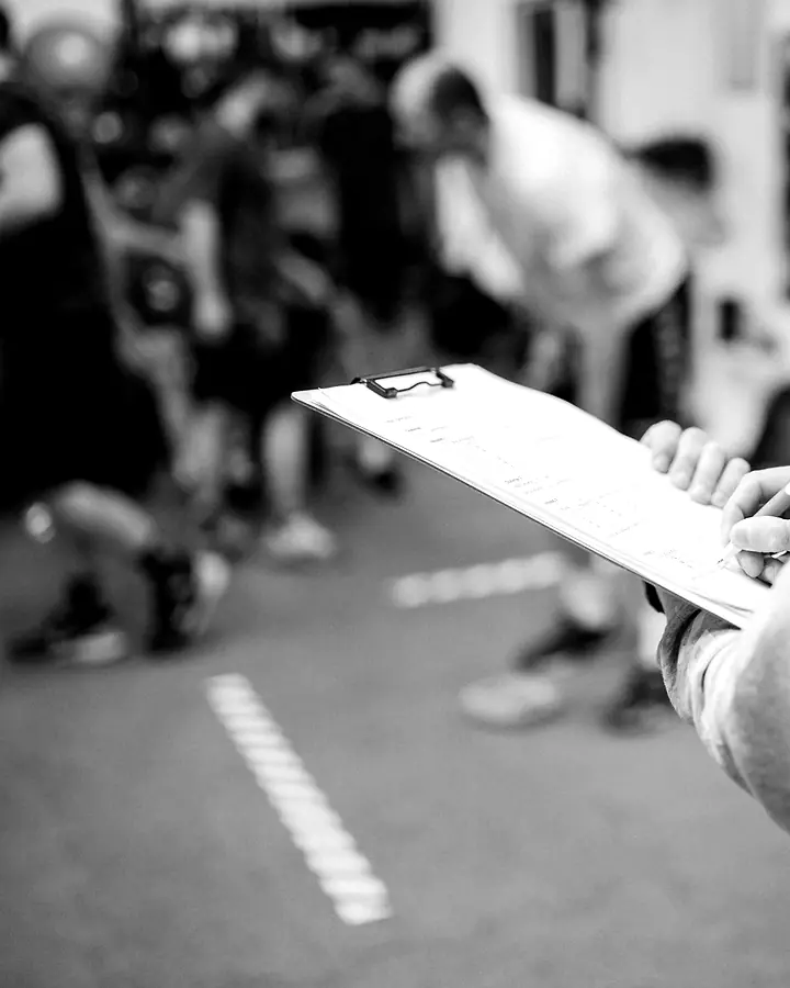 Trainer mit Klemmbrett beobachtet eine Trainingsgruppe.